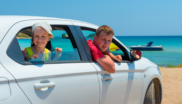 Vater und Kind mit Mietauto am Strand