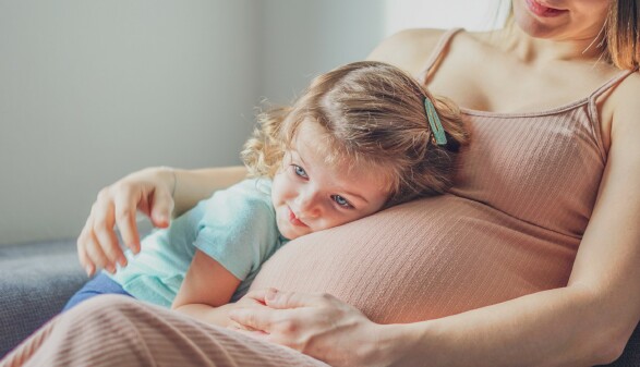  Kleines M&auml;dchen legt den Kopf auf den Bauch ihrer schwangeren Mama.