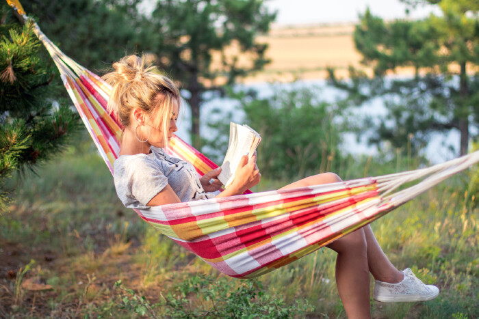 Junge Frau liegt in einer H&auml;ngematte im Gr&uuml;nen am See oder Fluss und liest ein Buch