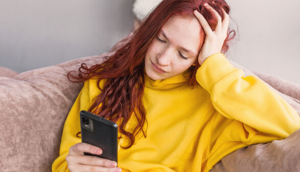 Frau sitzt auf der Couch und schaut ins Handy