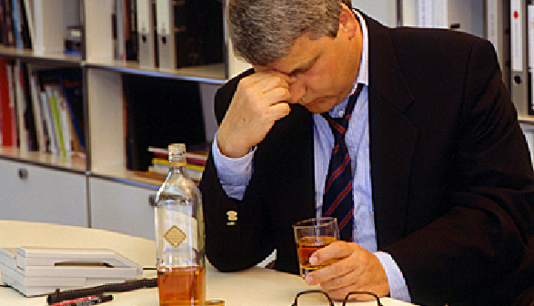 Mann sitzt mit einer Flasche Alkohol beim Schreibtisch © Udo Kroener, Fotolia