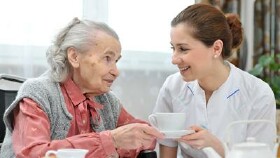 Junge Frau bedient eine alte Frau im Rollstuhl