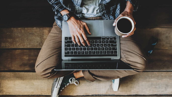 Mann sitzt mit Laptop und Kaffee am Boden