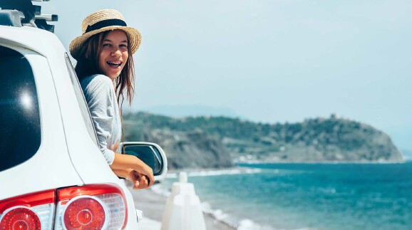 Auto fährt am Strand entlang. Mädchen lehnt sich aus dem Fenster