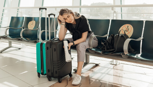 Müde Reisende sitzt mit Koffern im Wartebereich eines Flughafens