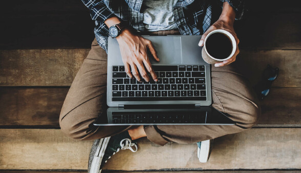 Mann sitzt mit Laptop und Kaffee am Boden