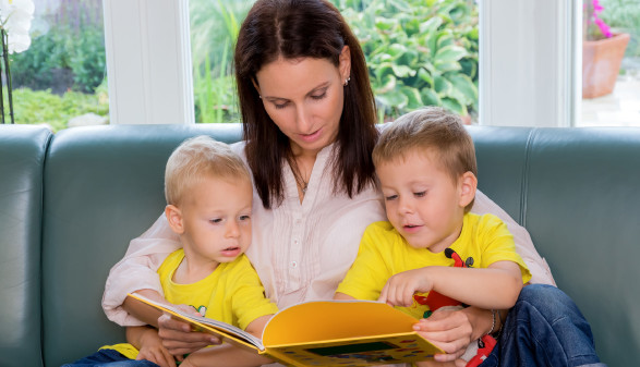 Mutter liest ihren 2 Kindern ein Buch vor